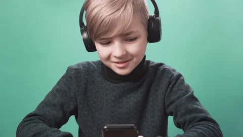 Young boy talking mobile phone with headphones over green background. Stock Footage 151734799