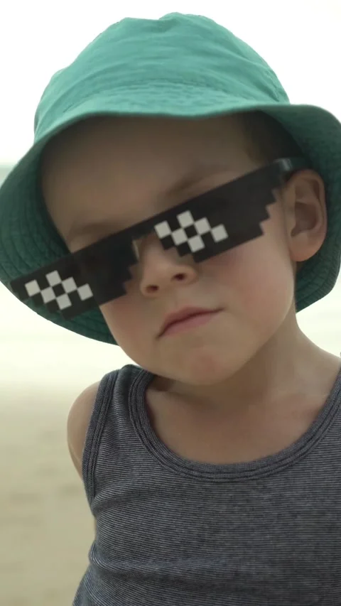 Young boy in a teal bucket hat and pixel sunglasses looks at the camera  Stock Footage 347101917