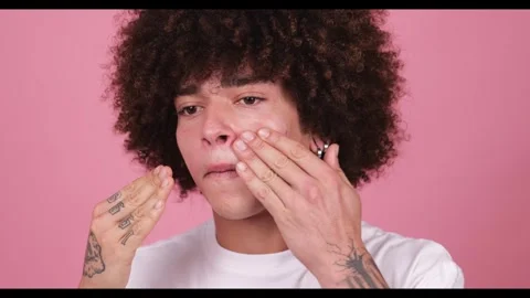 A young boy with a thick, wavy afro and tattoos on his fingers applies cream to Video stock 269137048
