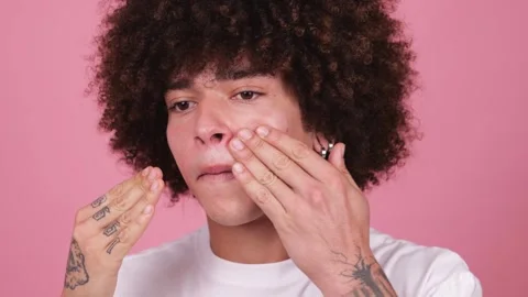 A young boy with a thick, wavy afro and tattoos on his fingers applies cream to Stock Footage 269363140