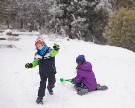 Young boy throws a snowball while a young girl makes more snowballs Foto stock