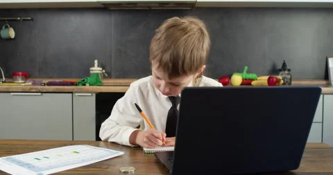 Young boy in tie writes in notebook with pencil near open laptop Video stock 314721957