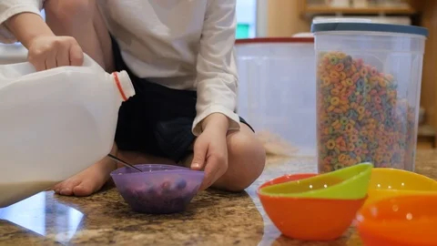 Young boy on top of kitchen counter pours a jug of milk into a bowl of cereal Stock Footage 86712708