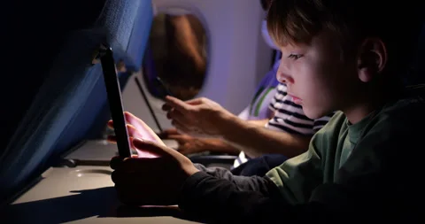 Young boy touch tablet screen then lean back on seat, nighttime flight Stock Footage 303992361