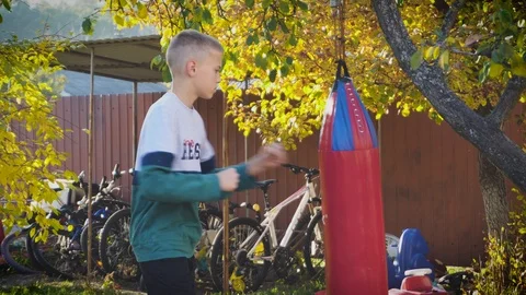 Young boy training with a big red punching bag. Sport activity outdoor at sunset Stock Footage 98377157
