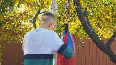 Young boy training with a big red punching bag. Sport activity outdoor at sunset Video stock 98377247