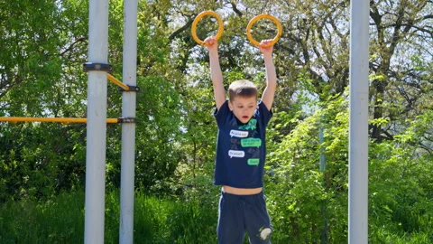 Young boy training on gymnastics rings, outdoor workout for kids strength Stock Footage 308032301