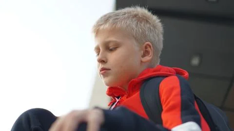 Young boy in training suit with backpack sitting and looking away. Stock Photos