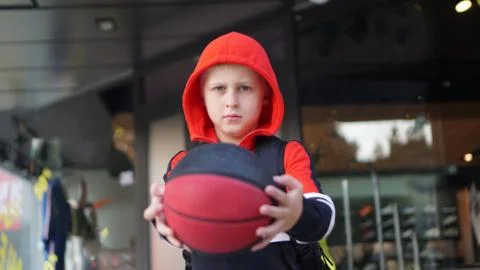 Young boy in training suit posing with basketball in front of store. 스톡 사진