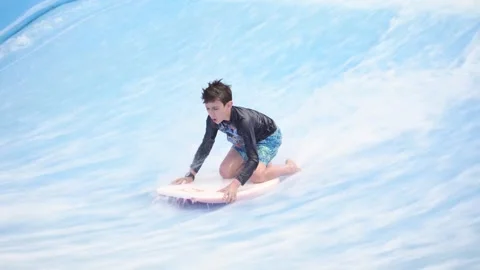 Young boy trains on an artificial surfing wave simulator. Stock Footage 346269962