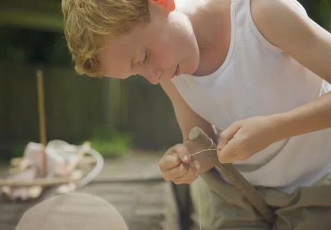 Young boy tying a knot with a string around a wooden stick Stock Photos