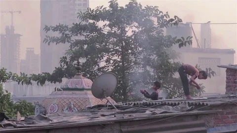 Young boy tying a thread on a kite as another flies a kite on a rooftop Video stock 72476183