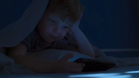 Young boy under blanket at night watching smartphone screen in dark bedroom Stock Footage 317234551