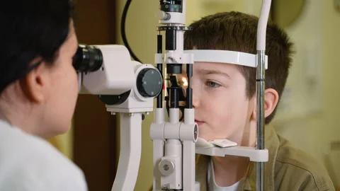 Young boy undergoing slit lamp eye exam by optometrist Stock Footage 310808421