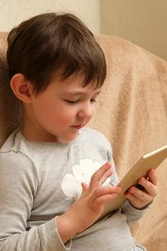 Young boy uses a digital tablet, focusing intently on the screen. Child engag Stock Photos