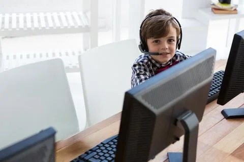 Young boy using computer and headset in office, engaging in online learning.. Stock Photos