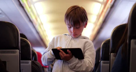 Young boy using digital tablet on airplane flight, stand in aisle 스톡 동영상 324862108