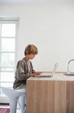 Young Boy Using Laptop At Kitchen Table Stock Photos