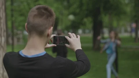 Young Boy Using Smart Phone To Filmmaking Friends While Playing Volleyball. 4K. Stock Footage 107238702
