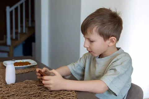 Young boy using smartphone at breakfast table. A young boy sits at a dining Stock Photos