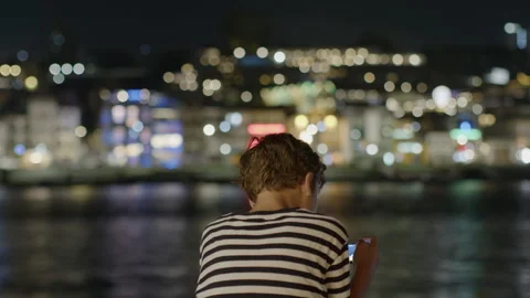 Young boy using smartphone in front of blurred city lights at night Stock-Footage 300580162