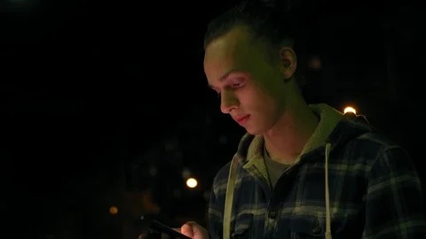 Young boy using smartphone outdoors at night, milticolor screen light, 4k 6 Видео 95425324
