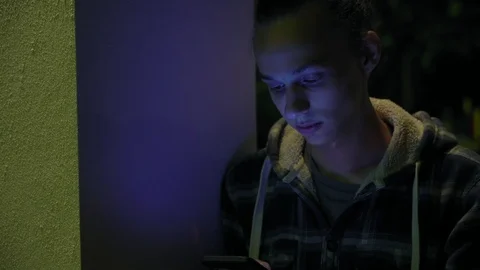 Young boy using smartphone outdoors at night, milticolor screen light, 4k 5 Vidéo 95425332