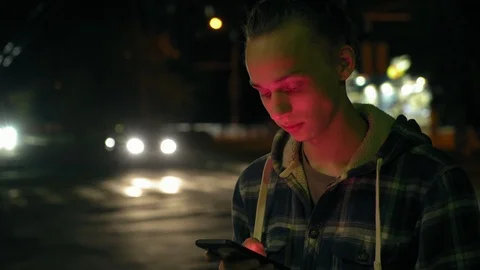 Young boy using smartphone outdoors at night, milticolor screen light, 4k 3 Vidéo 95425360