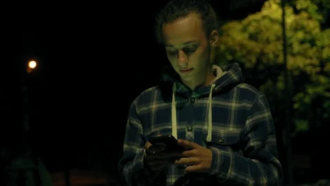 Young boy using smartphone outdoors at night, milticolor screen light, 4k 2 動画素材 95425770