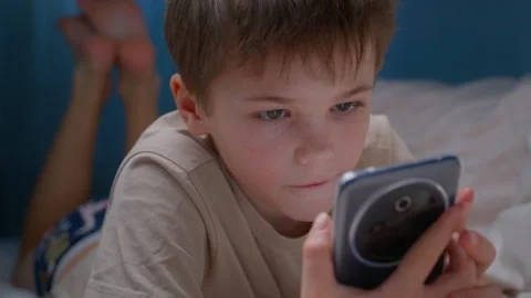 Young boy using smartphone while lying in bed Stock Footage 325736237