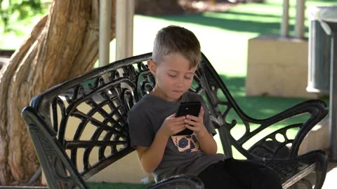 Young Boy Using Smartphone While Sitting on Park Bench Stock Footage 340336318