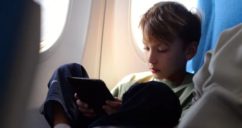 Young boy using tablet on airplane, sitting focused on device Stock Footage 303994423