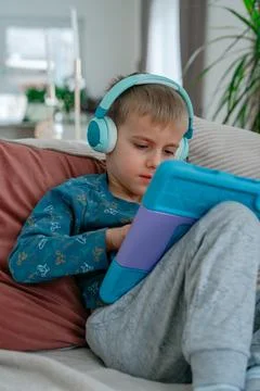 Young boy using tablet with headphones while sitting on sofa. Fotos de archivo