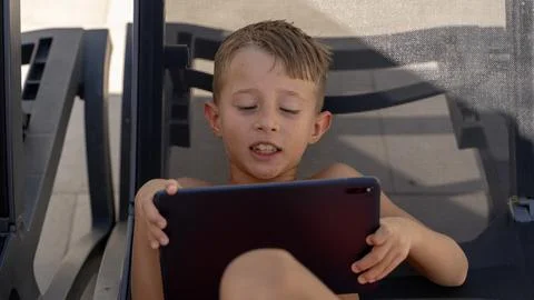 Young Boy Using Tablet While Sitting on Outdoor Lounge Chair 스톡 사진
