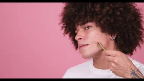 A young boy with a voluminous wavy afro uses a green jade roll on his jawline 스톡 동영상 269136882