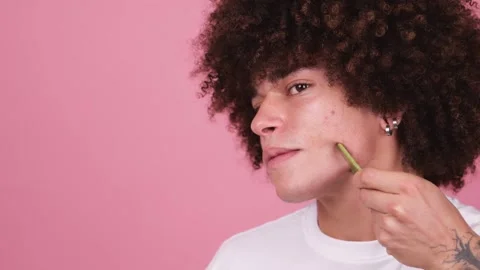A young boy with a voluminous wavy afro uses a green jade roll on his jawline Stock Footage 269362790