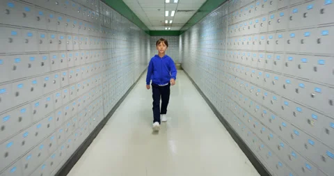 Young boy walk towards camera in long hall with many small post boxes Stock Footage 322099125