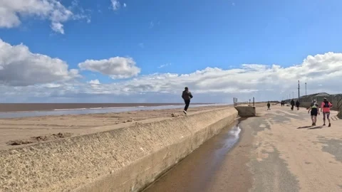 Young boy walking along a wall on the seafront by the beach on a stormy sun.. Stock Footage 240286019
