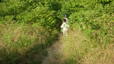 Young Boy Walking Away Through Lush Green Pathway with Adult Following Video stock 339085370