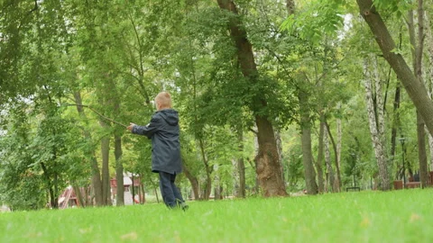 Young boy walking in park preparing for back to school, green trees, wet grass Stock Footage 345167271