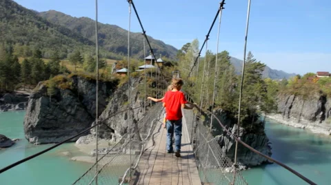 Young boy walking  through a rope bridge over the river in mountains Stock Footage 55633339