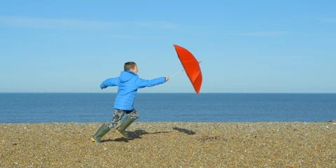 A young boy walking on a winters beach opens his umbrella and gets blown away! Video stock 86423523