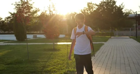 Young boy walks with school backpack through park at sunset. Student moves Stock Footage 345787207