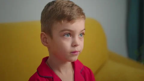 Young boy watching intently while sitting on a yellow sofa at home 스톡 동영상 303801603
