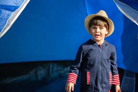 A young boy wearing a blue jacket and a straw hat stands in front of a blue.. Stock Photos