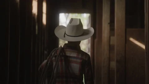 Young Boy Wearing a Cowboy Hat and Carrying a Rope Through Stables Stock Footage 208769767