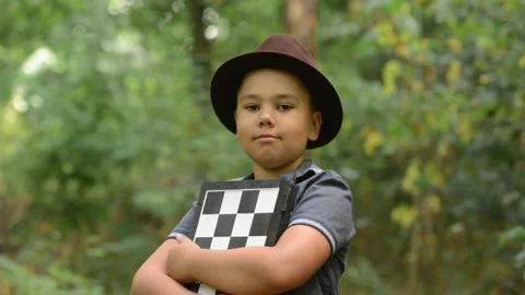 Young Boy Wearing Hat Holding Chessboard Confidently Outdoors Vídeos de archivo 343550242