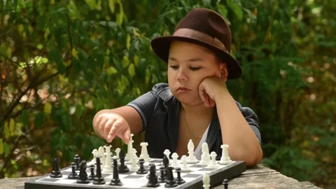 Young Boy Wearing Hat Playing Chess and Making Move Outdoors Video stock 343550237