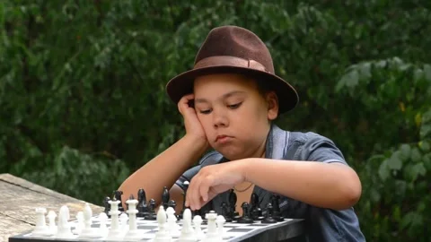 Young Boy Wearing Hat Plays Chess and Makes a Move in Forest Outdoors Video stock 343550249