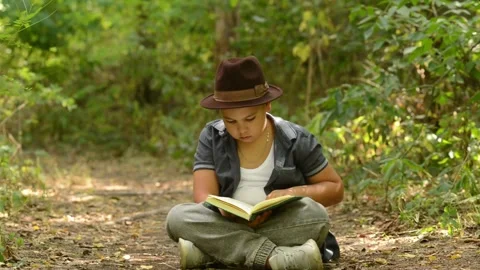 Young Boy Wearing Hat Sitting and Reading Book Outdoors in Forest Stock-Footage 343550246